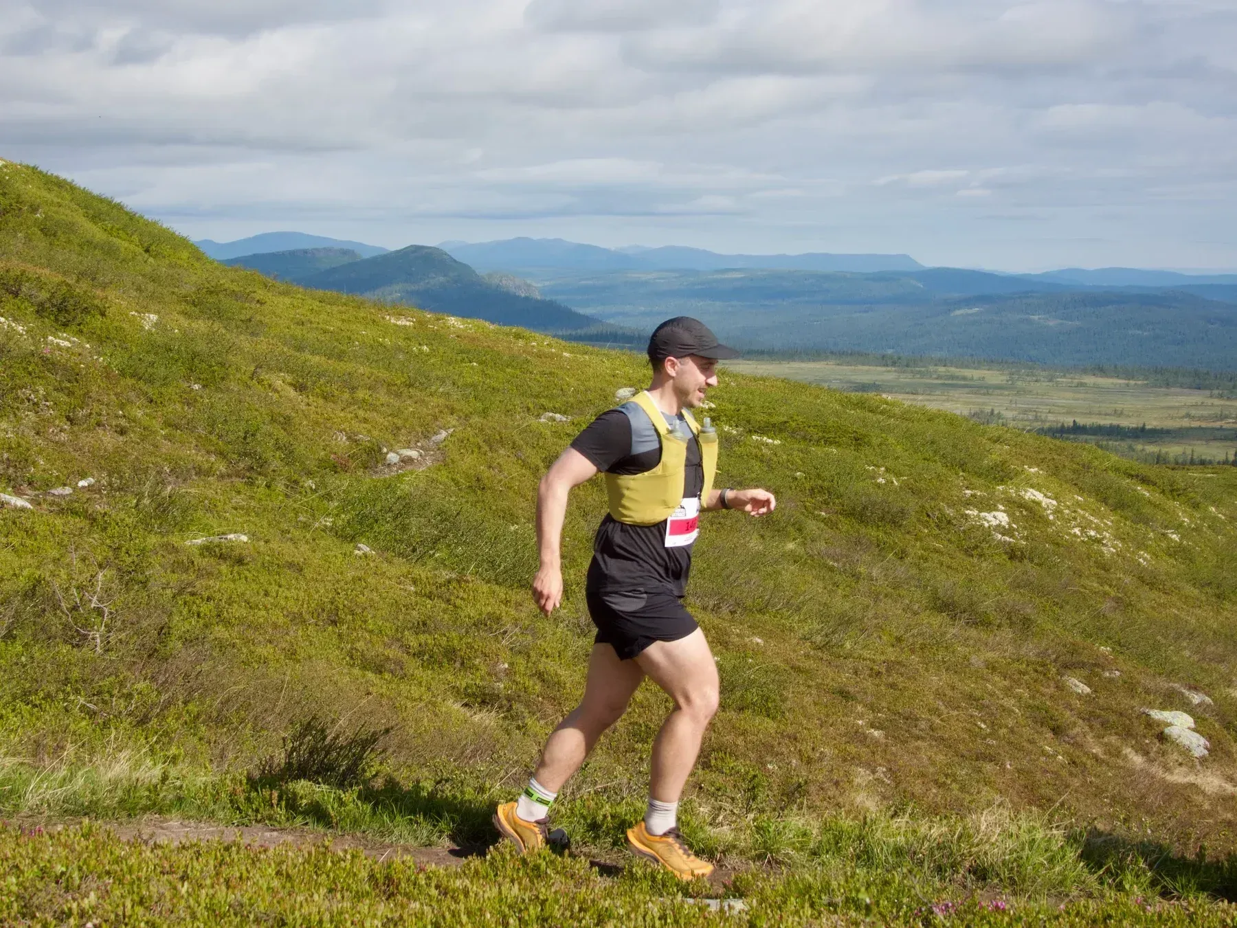 Løper med gul vest på en gresskledd fjellsti.