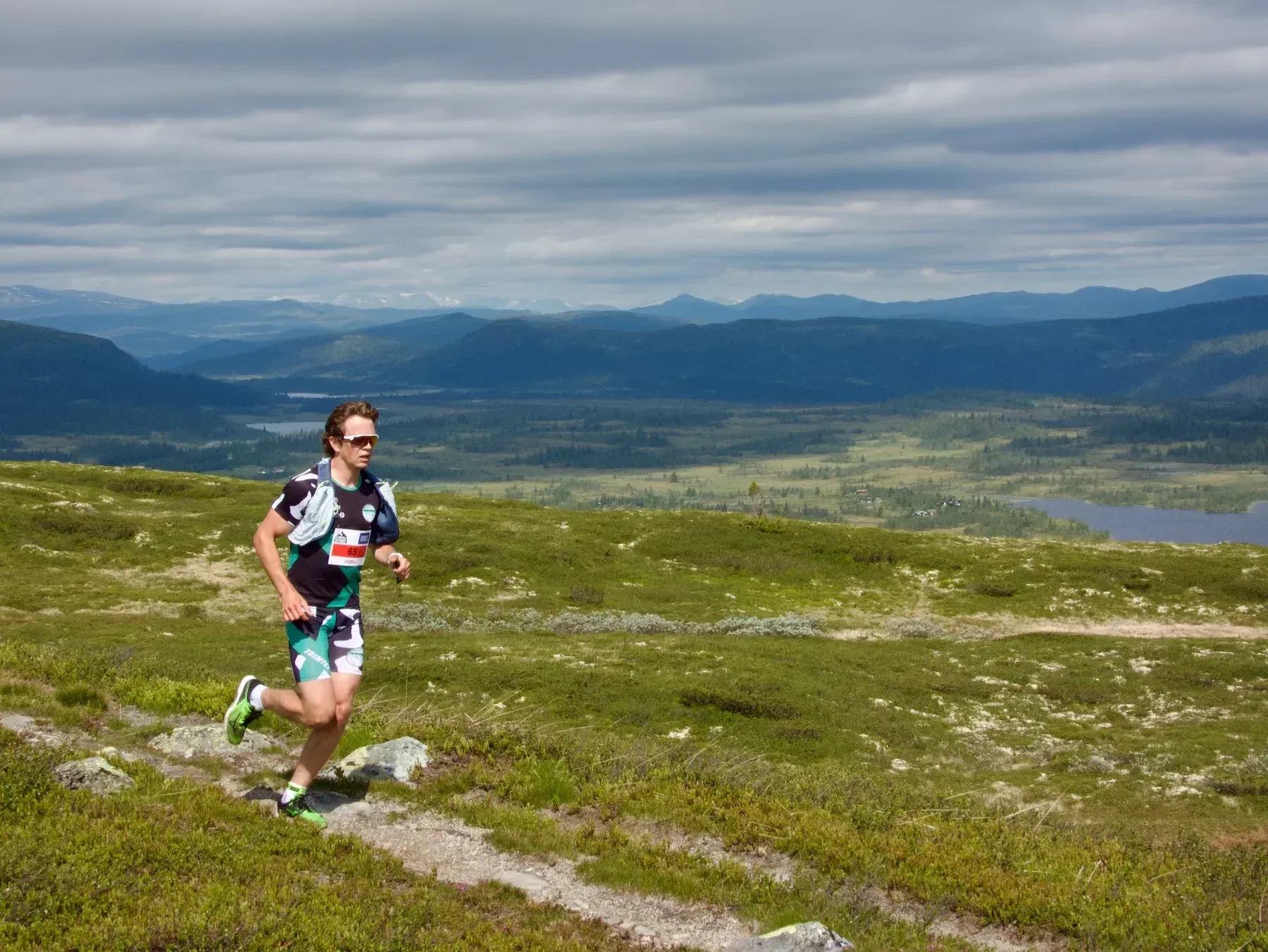Løper med solbriller på sti over grønne fjell.