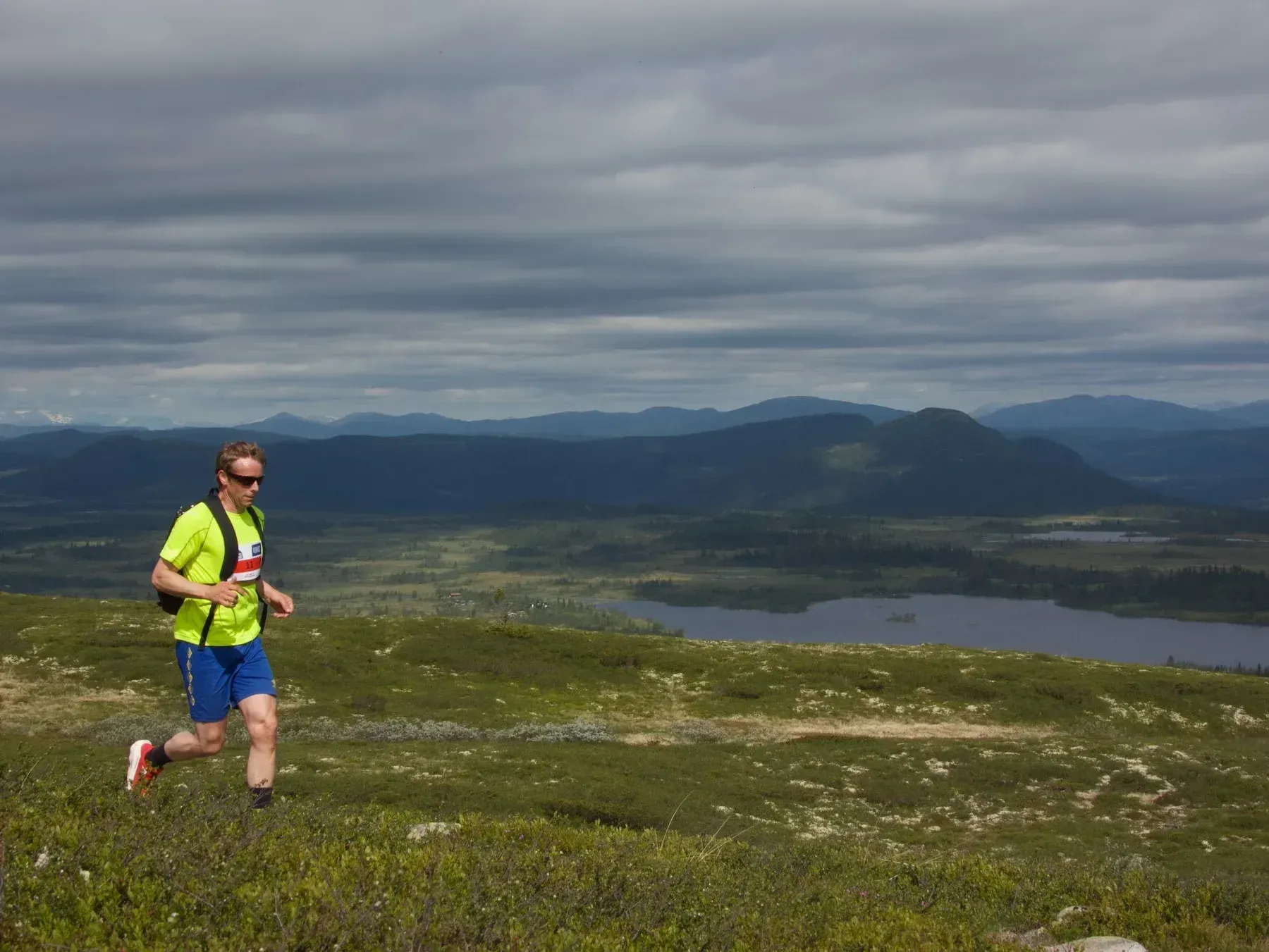 Løper i gul trøye og blå shorts med dalen i bakgrunnen.