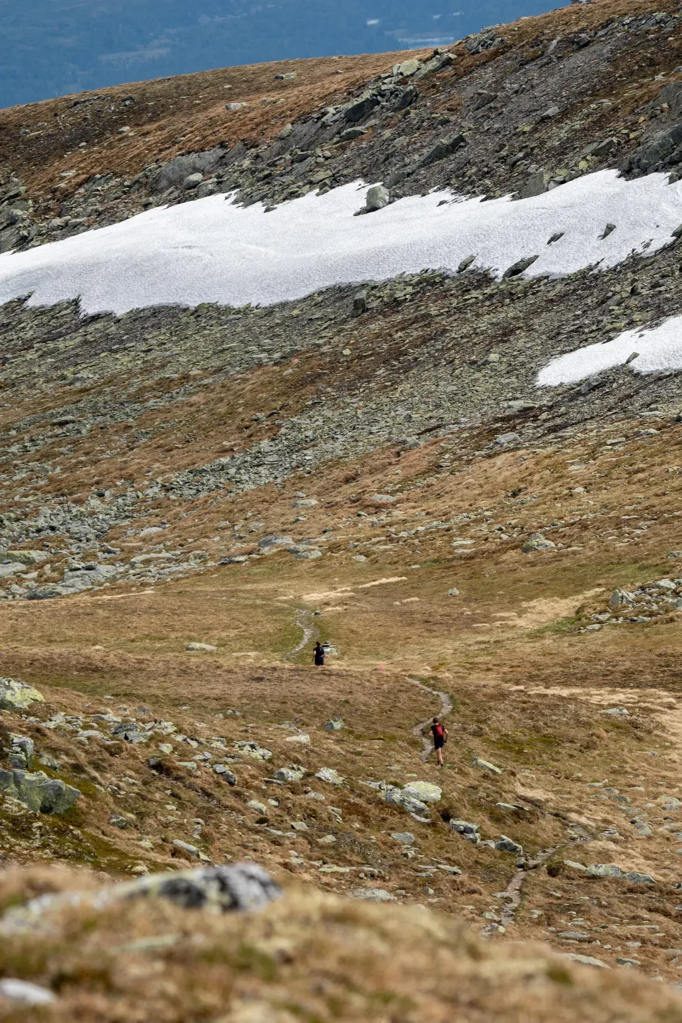 Løpere på en smal sti gjennom en steinete fjellside med snøpartier