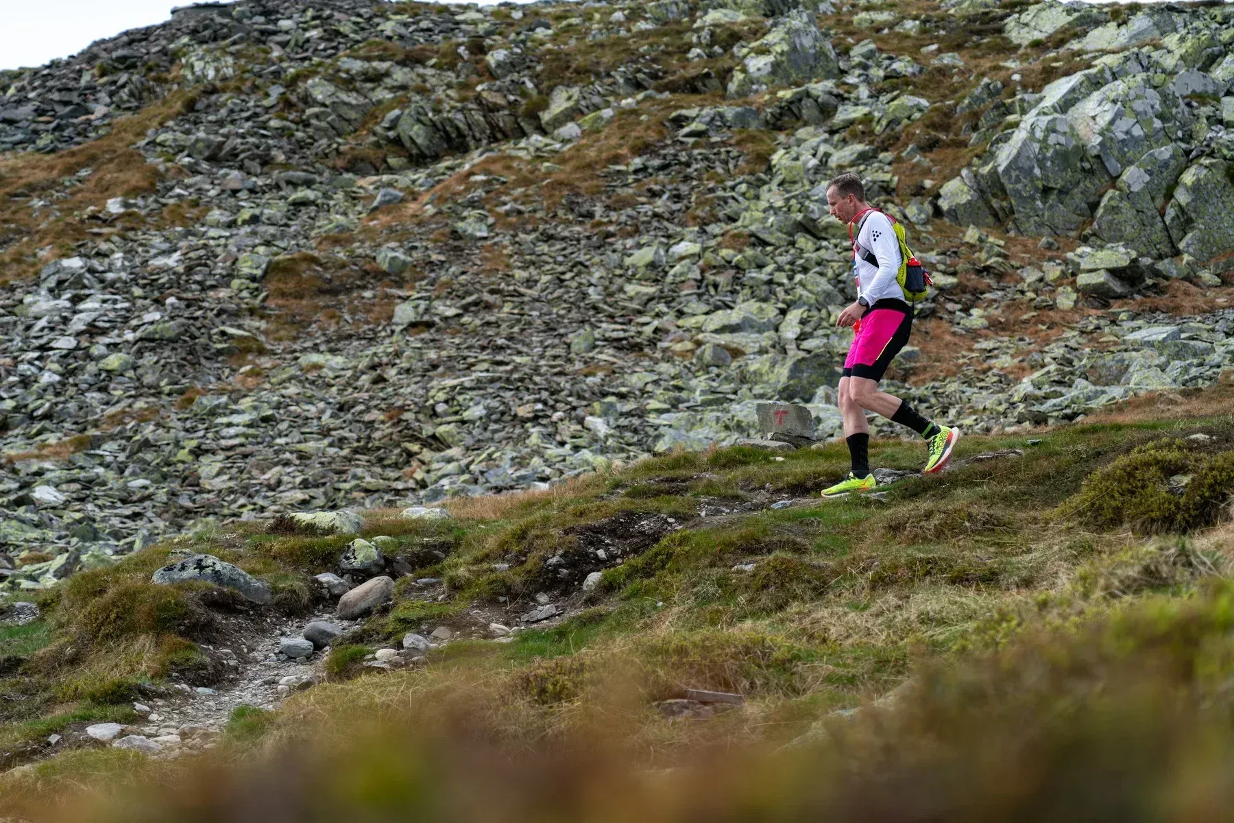 Løper med rosa shorts passerer en bratt steinur.