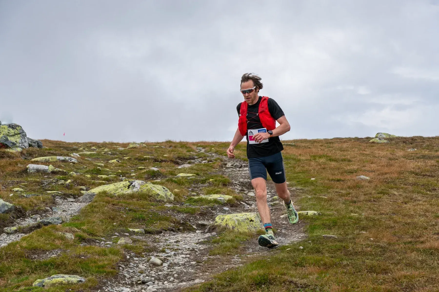 Løper med rød vest på en smal sti over fjellvidda.
